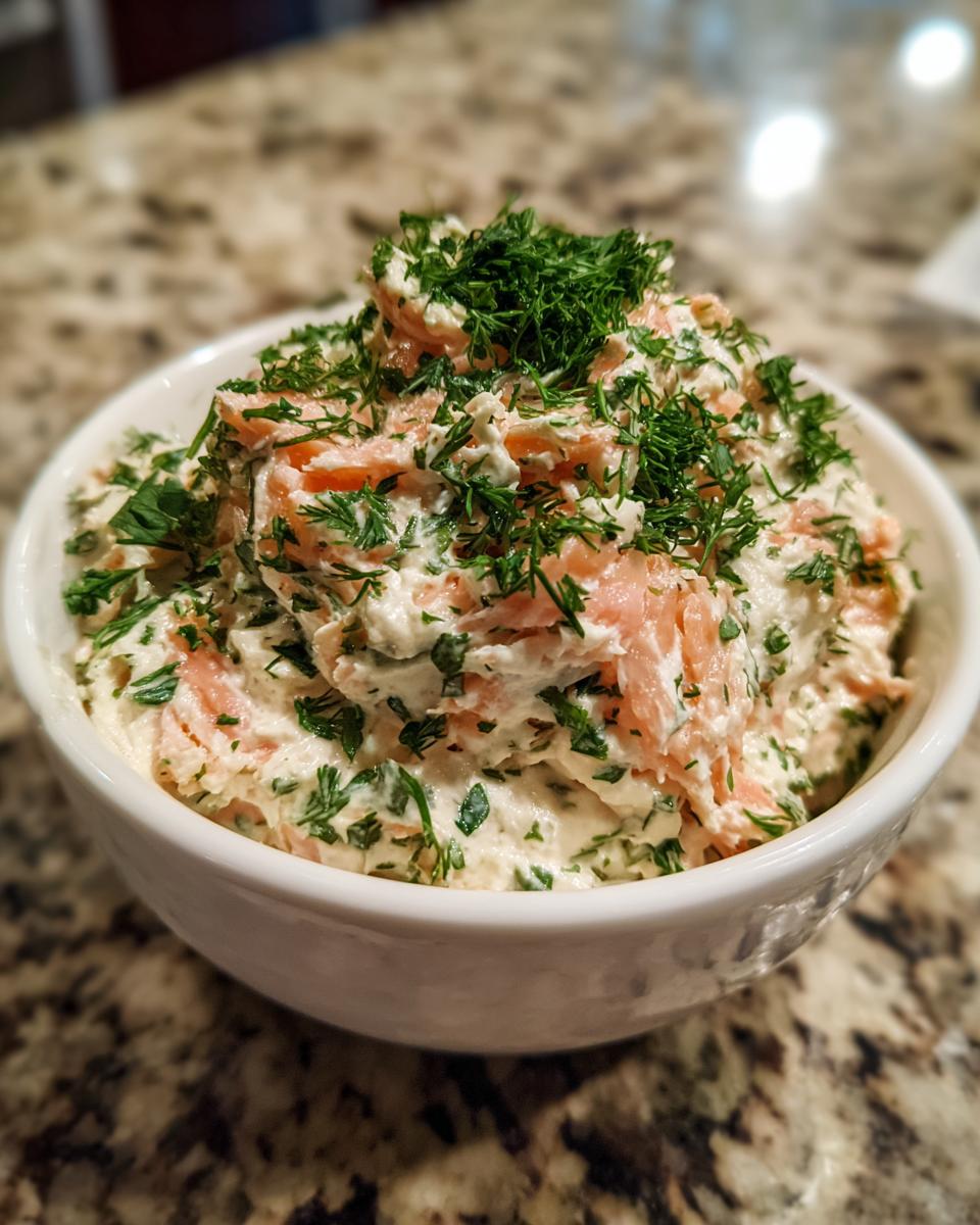 A close-up of creamy salmon dip mixed with herbs, topped generously with fresh dill.