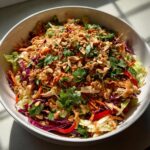 A vibrant bowl of amazing thai chicken salad topped with crushed peanuts and fresh cilantro.