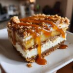 A decadent slice of apple pie cheesecake topped with spiced apples, crumble, and rich caramel sauce.