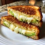 A close-up of a perfectly grilled avocado mozzarella grilled cheese sandwich, with melted cheese oozing out.