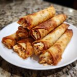 A stack of crispy, golden-brown baked chicken taquitos filled with shredded chicken.