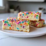 Close-up of three Birthday Cake Protein Bars topped with colorful sprinkles on a white plate.
