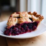 Close-up of a juicy slice of blackberry pie featuring a golden lattice crust and rich, dark berry filling.