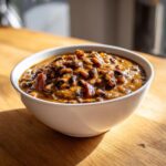 A close-up of a white bowl filled with rich, savory black eyed peas stewed with meat pieces.