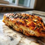 Close-up of a perfectly cooked brined herb chicken breast, golden brown with visible herbs.