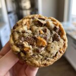 Close-up of a homemade Butterfinger Caramel Crunch Cookie loaded with chocolate chips and Butterfinger pieces.
