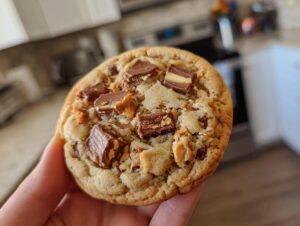 A close-up of a delicious Butterfinger Caramel Crunch Cookie, loaded with chocolate and candy pieces.