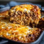 A fork lifting a cheesy slice of Cajun cabbage casserole with ground beef and cabbage.