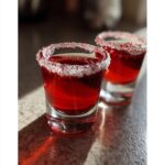 Two vibrant red cherry shots, each with a sugar-rimmed glass, ready for a party.