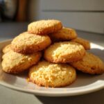 A close-up shot of a pile of golden-brown Christmas shortbread cookies on a white plate.