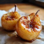 Two halves of cinnamon maple baked pears, glistening with syrup and topped with nuts.