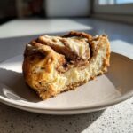 A delicious slice of cinnamon roll cheesecake on a plate, showcasing the swirl of cinnamon and creamy cheesecake.
