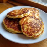 A close-up of a stack of golden-brown cottage cheese pancakes on a white plate, ready to be served.