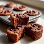 Close-up of fudgy cottage cheese protein brownie bites, some stacked and one cut in half, topped with chocolate chips.