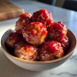A close-up shot of a bowl filled with glistening cranberry meatballs, coated in a rich, red sauce.