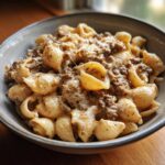 A close-up of a bowl filled with creamy beef and shells pasta, topped with melted cheese.