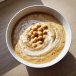 Overhead view of a bowl of creamy chickpea soup, swirled with cream and topped with whole roasted chickpeas.
