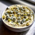 Close-up of a creamy dirty martini dip topped with blue cheese crumbles and sliced green olives.