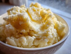 Close-up of fluffy mashed potatoes in a white bowl, topped with melting butter.