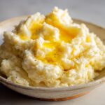 A close-up of a bowl of creamy mashed potatoes topped with melted butter and black pepper.