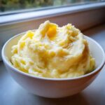 A close-up of a bowl filled with fluffy, creamy mashed potatoes topped with melted butter.