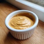 Close-up of thick, creamy peanut sauce swirled in a small white ramekin, ready for dipping.