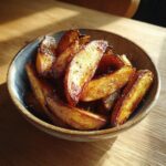 A rustic bowl filled with golden brown, crispy potato wedges seasoned with salt.
