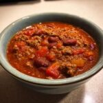 A close-up of a bowl filled with hearty crock pot chili, featuring ground beef, kidney beans, and tomatoes.