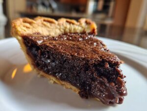 Close-up of a rich, dark slice of hot fudge pie showing the fudgy filling and flaky crust.