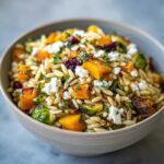 A close-up of a bowl of fall orzo salad filled with roasted butternut squash, Brussels sprouts, cranberries, and feta cheese.