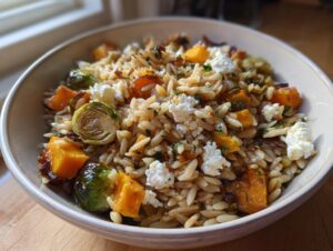 A close-up of a bowl of fall orzo salad featuring roasted butternut squash, Brussels sprouts, and crumbled feta cheese.