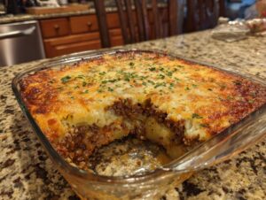 A hearty ground beef and potato casserole baked in a glass dish, topped with melted cheese and parsley.