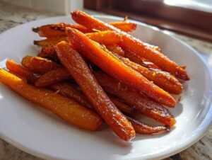 A close-up of beautifully caramelized honey glazed carrots piled high on a white serving dish.