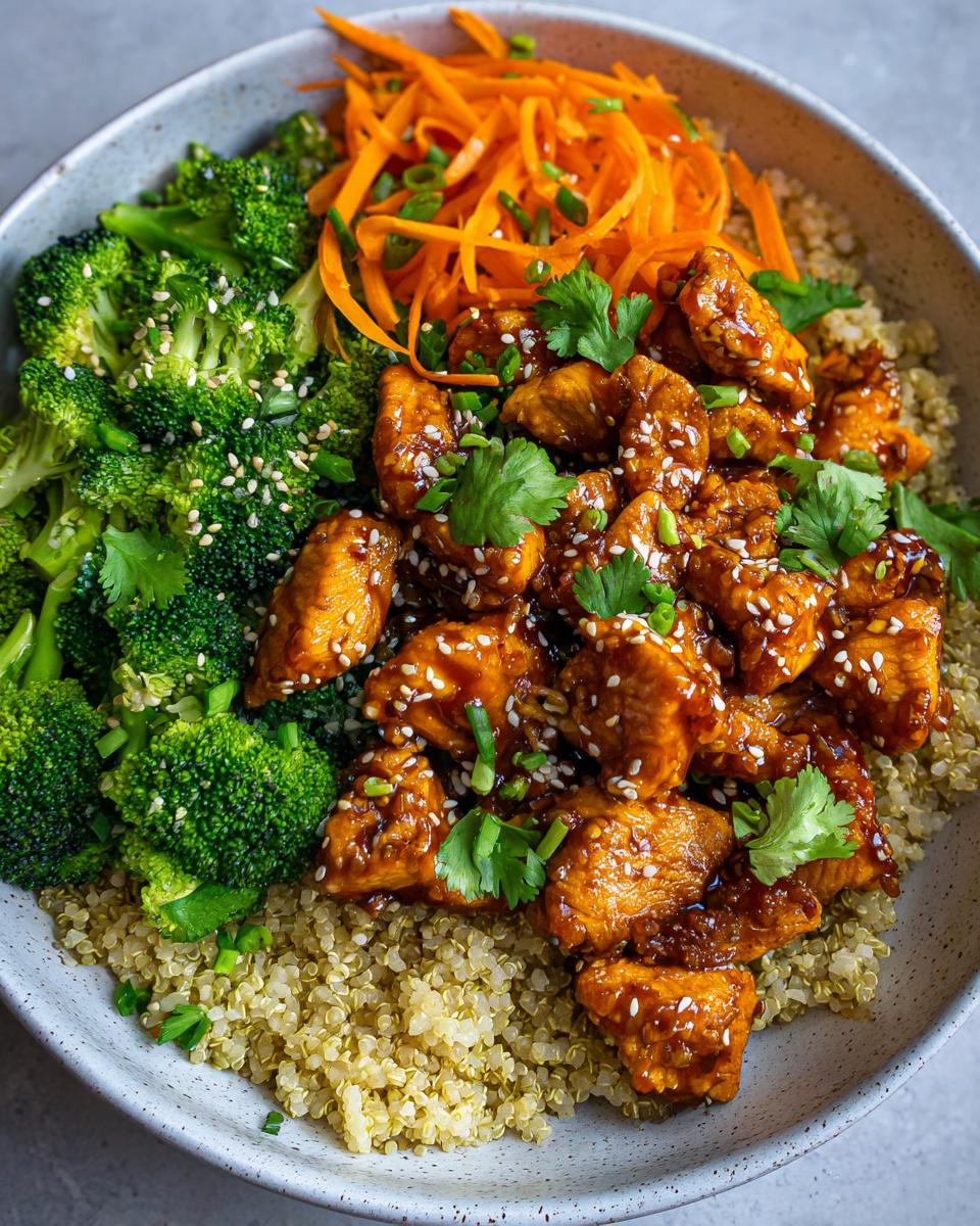 A close-up of a hot honey chicken bowl featuring glazed chicken, steamed broccoli, shredded carrots, and quinoa.