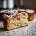 A close-up of a slice of rustic Italian apple cake (torta di mele) dusted with powdered sugar.