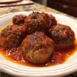 Close-up of tender Italian meatballs simmered in a rich tomato sauce, sprinkled with herbs.