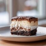 Close-up of a rich, layered slice of italian love cake featuring a dark base, white cream, and chocolate ganache topping.