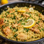 A close-up of a skillet filled with lemon chicken orzo, garnished with lemon slices and fresh parsley.