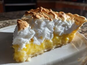 A close-up slice of lemon meringue pie showing thick, bright yellow filling and fluffy, toasted meringue.