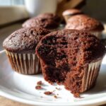 A close-up view of a moist chocolate cupcake, with a bite taken out, revealing its fluffy interior.