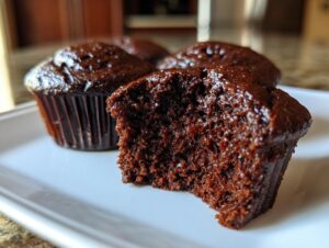 Close-up of a moist chocolate cupcake with a bite taken out, showing its rich texture.