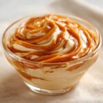 A close-up of a glass bowl filled with creamy no-bake caramel cream, swirled with rich caramel sauce.