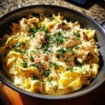 Close-up of a skillet filled with creamy one-pan chicken and buttered noodles, garnished with parsley and Parmesan cheese.