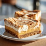 Close-up of two delicious pumpkin cheesecake bars with a creamy white swirl topping on a white plate.