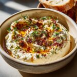 Close-up of creamy Pumpkin Whipped Feta Dip topped with fresh herbs, chili flakes, and olive oil.
