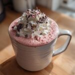 A mug of pink ruby hot chocolate topped with whipped cream and chocolate shavings.
