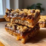 A close-up stack of two delicious salted caramel chocolate chip oat cookie bars, showcasing gooey caramel and chocolate chips.