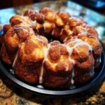 A golden-brown sourdough discard monkey bread, drizzled with a sweet white glaze, baked in a bundt pan.