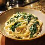 A close-up of a bowl filled with creamy spinach alfredo pasta, featuring fettuccine noodles and wilted spinach.