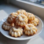 A plate piled high with freshly baked, star-shaped butter cookie treats dusted with powdered sugar.
